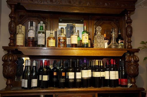 Wooden bar shelf displaying various bottles of spirits and wines, with intricate carvings and a warm ambiance.