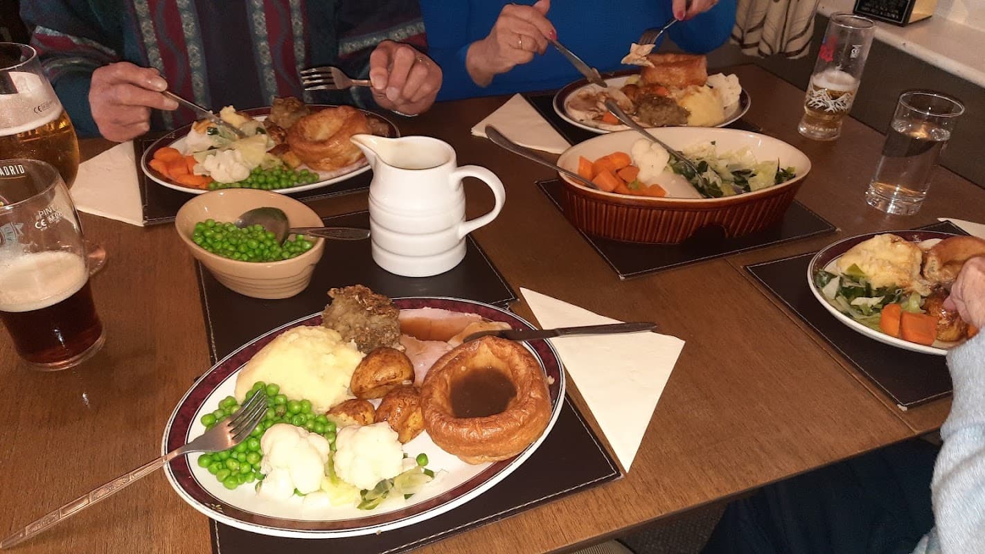 A table with plates of traditional British pub food, including roast dinner, vegetables, and drinks.