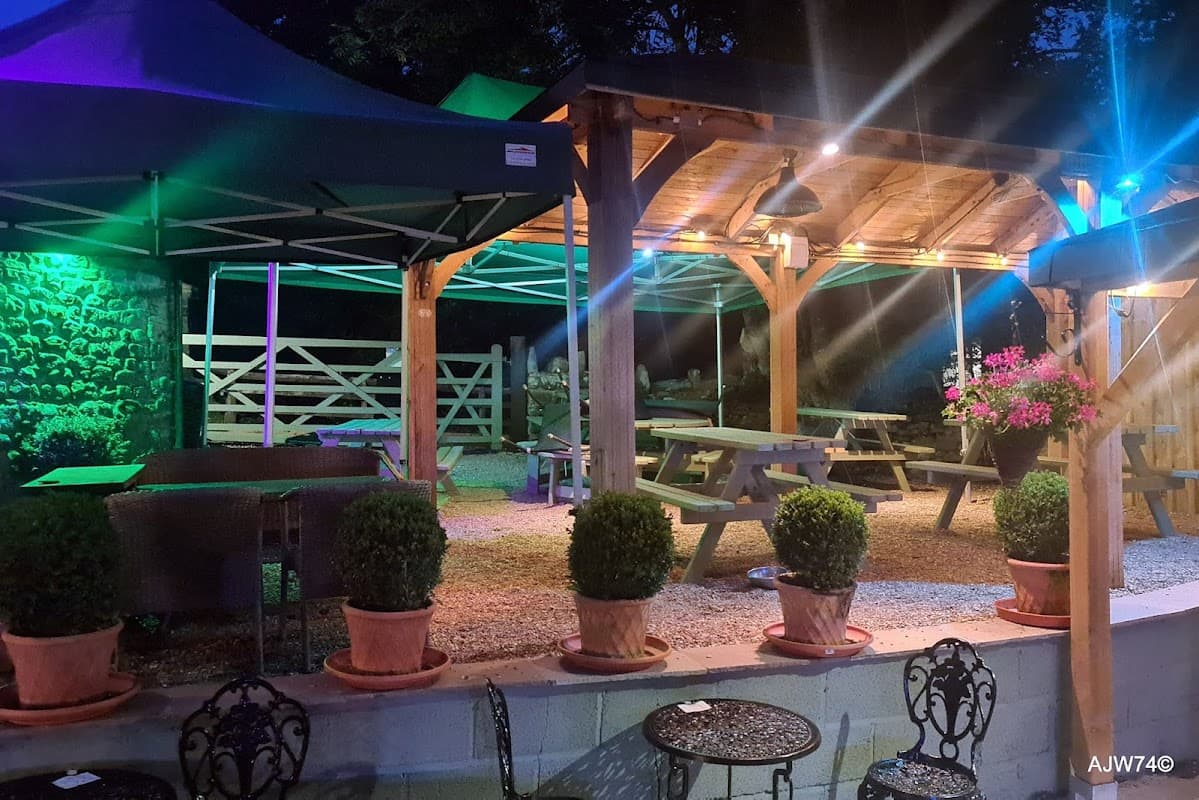 Outdoor dining area at The Blacksmiths Arms, featuring wooden tables, green canopies, and illuminated plants at night.