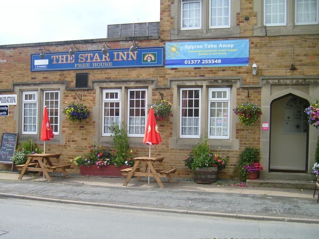 The Star Inn features outdoor seating with red umbrellas, flower baskets, and a welcoming entrance in a quaint Yorkshire village.