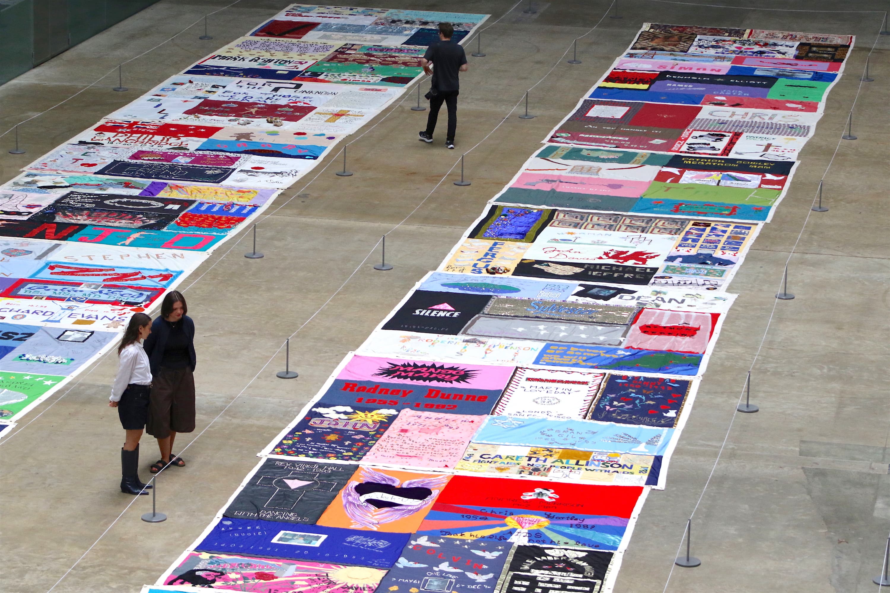 Colorful quilt panels displayed on a museum floor with visitors