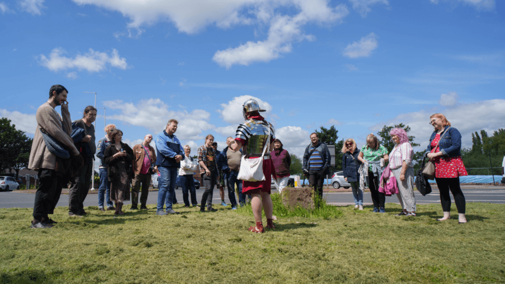Guide in Roman armor speaking to tourists on grassy area