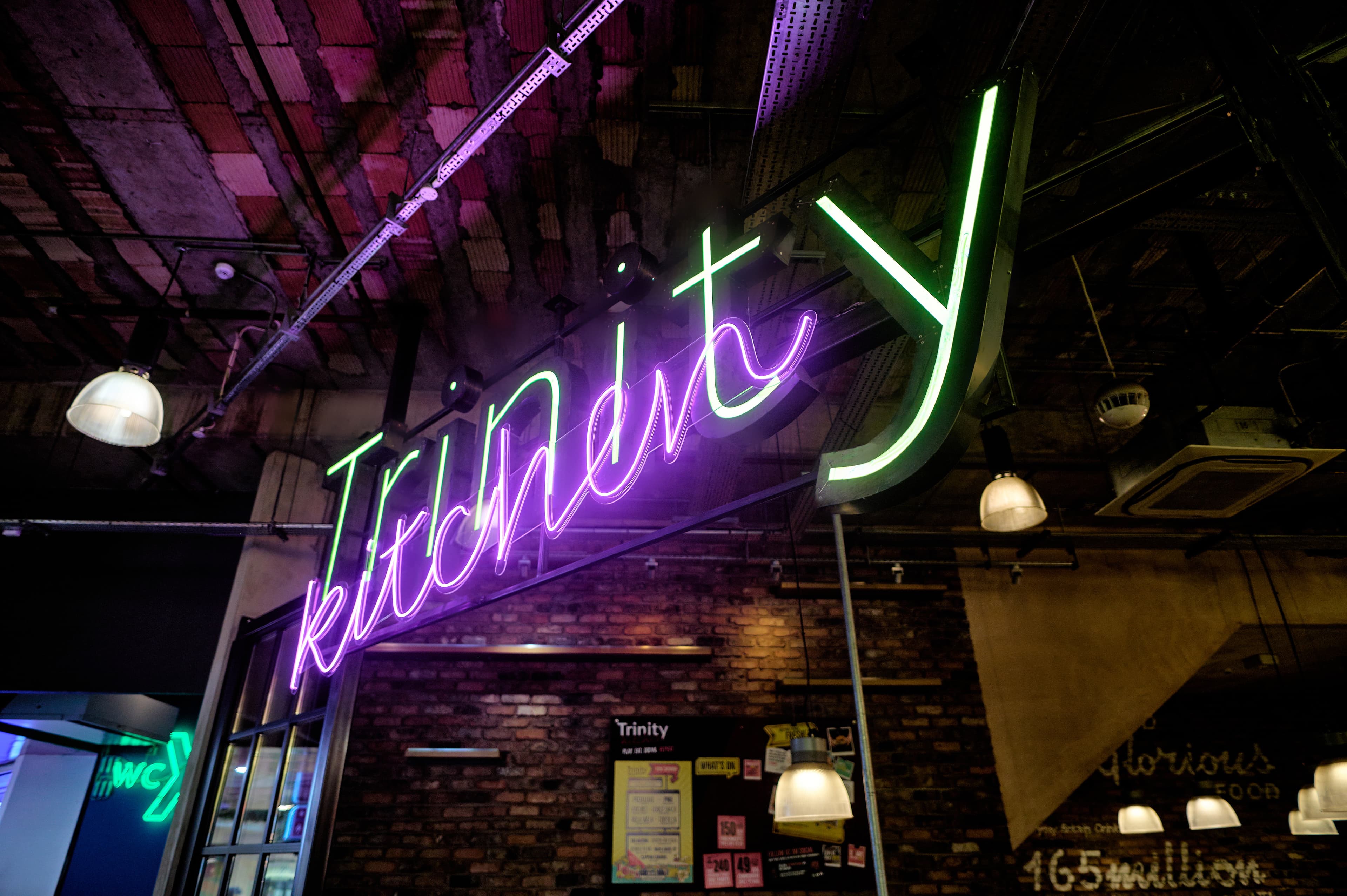 Neon sign for Trinity Kitchen in vibrant colors on brick wall