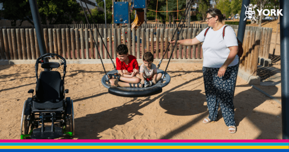 Children on swing in accessible playground with adult nearby