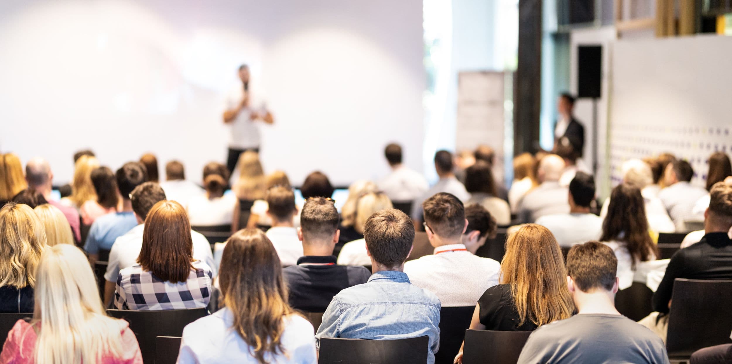 Audience seated in a modern conference room listening to a speaker