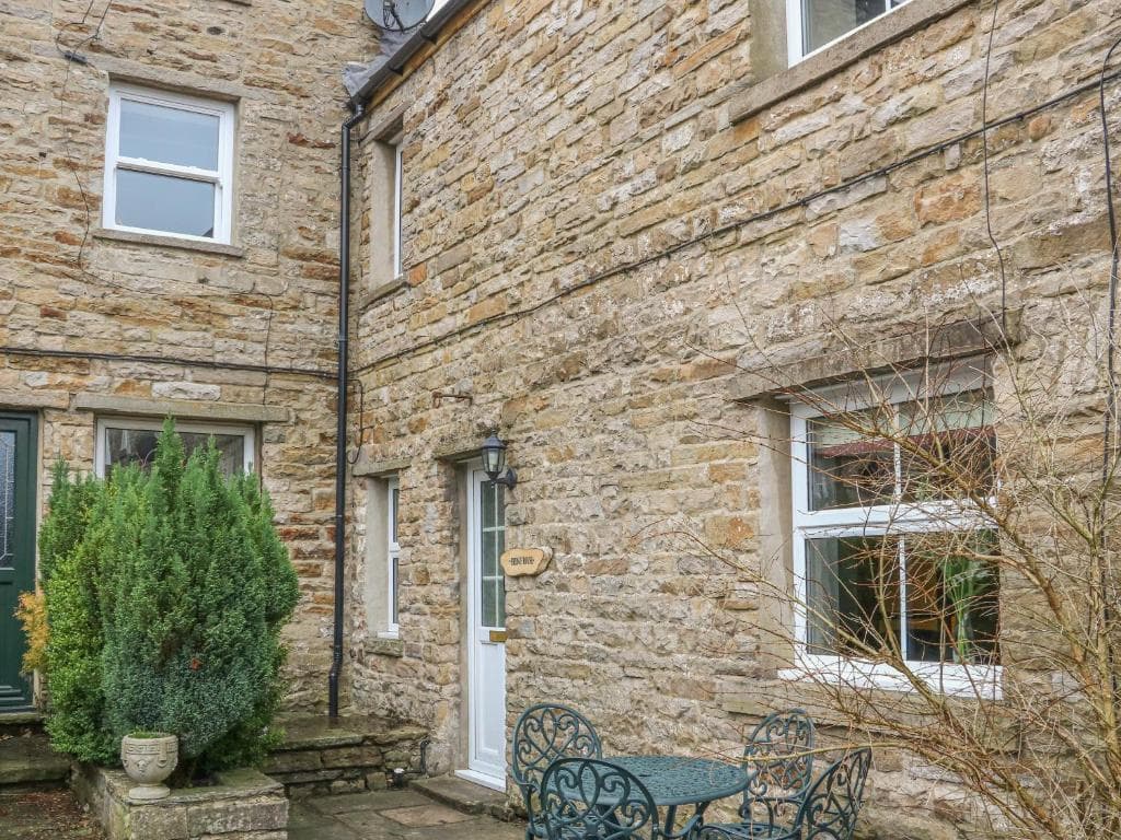 Stone cottage with ivy, white-framed windows, and a small patio featuring a wrought iron table and chairs.
