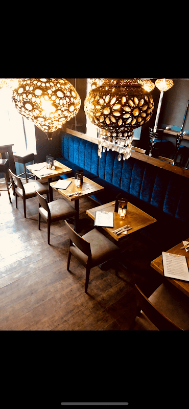 Cozy restaurant interior with wooden tables, chairs, blue velvet seating, and ornate hanging lights.