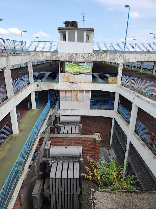 Abandoned multi-level car park with blue railings, a control tower, and overgrown plants in Bradford, Yorkshire.