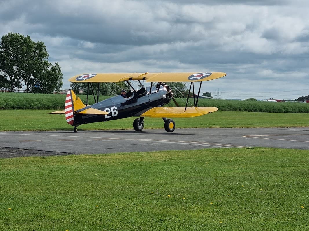 A vintage biplane with a yellow wing and black body taxis on a grassy airstrip at Breighton Aerodrome.