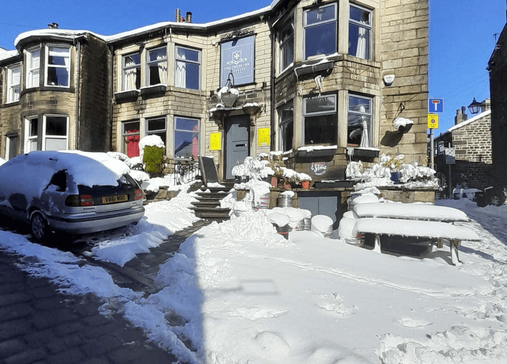 The Cross Inn bar covered in snow, with a parked car and outdoor seating visible in a winter scene.