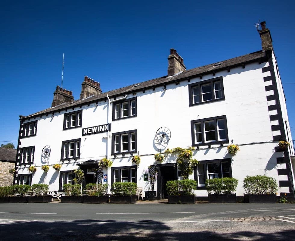 White building with black trim, large windows, flower boxes, and a sign reading "NEW INN" under a clear blue sky.