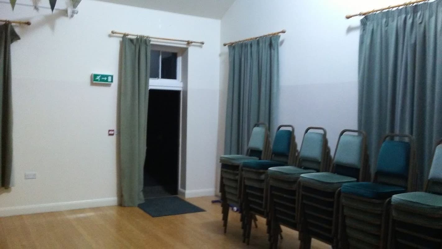 Interior of Gisburn Festival Hall featuring stacked chairs, curtains, and an open door.