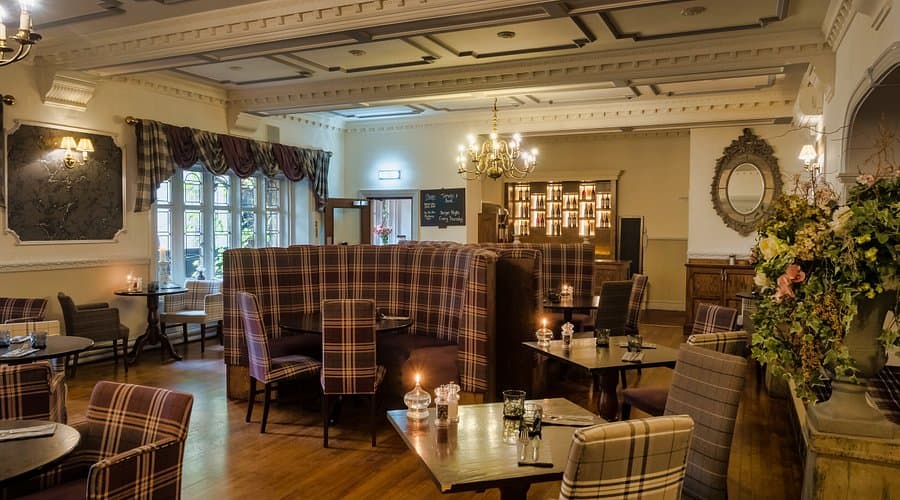 Elegant dining area with plaid seating, wooden tables, chandeliers, and floral arrangements in a cozy atmosphere.