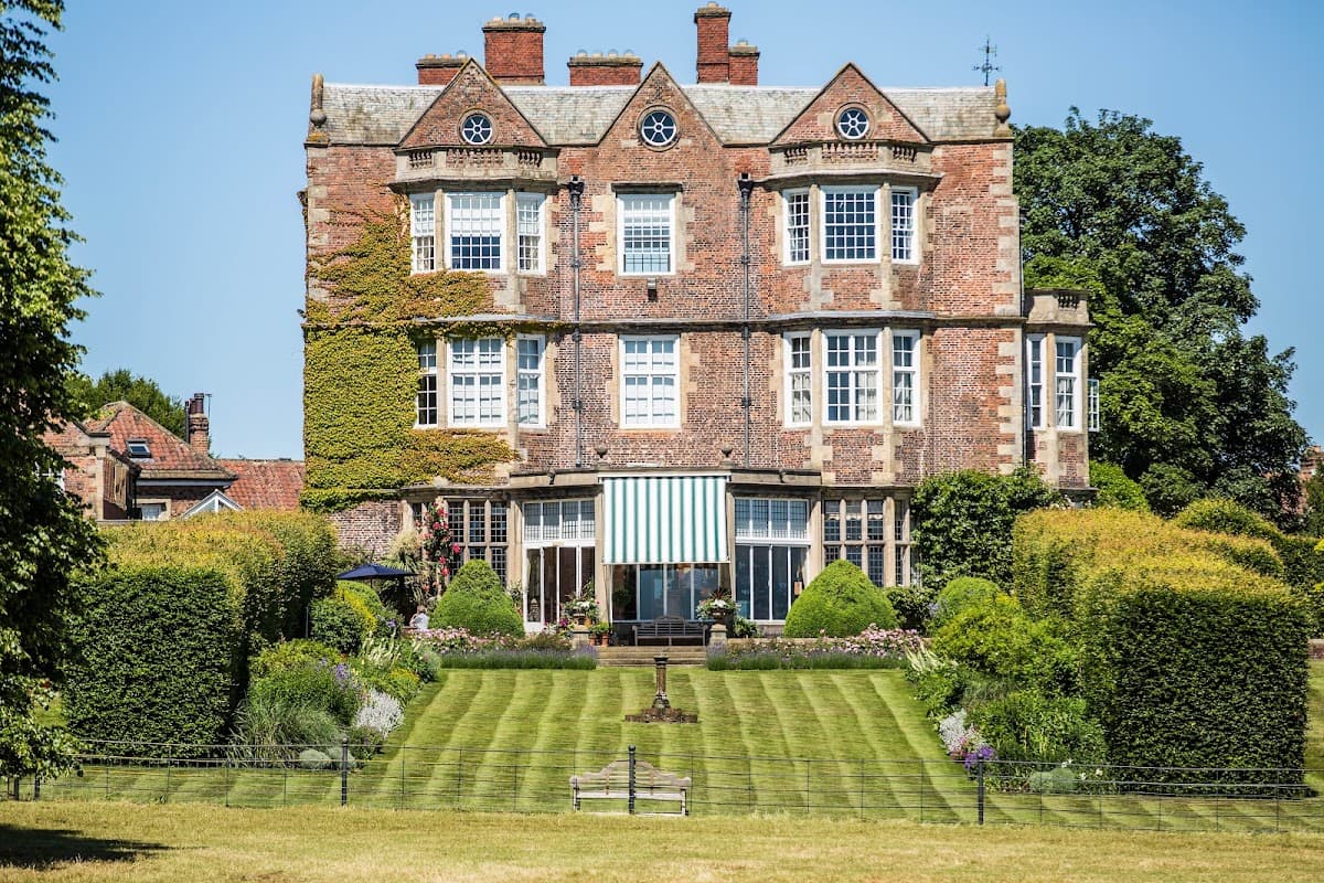 Elegant brick mansion with large windows, surrounded by lush gardens and neatly trimmed hedges in Goldsborough, Yorkshire.