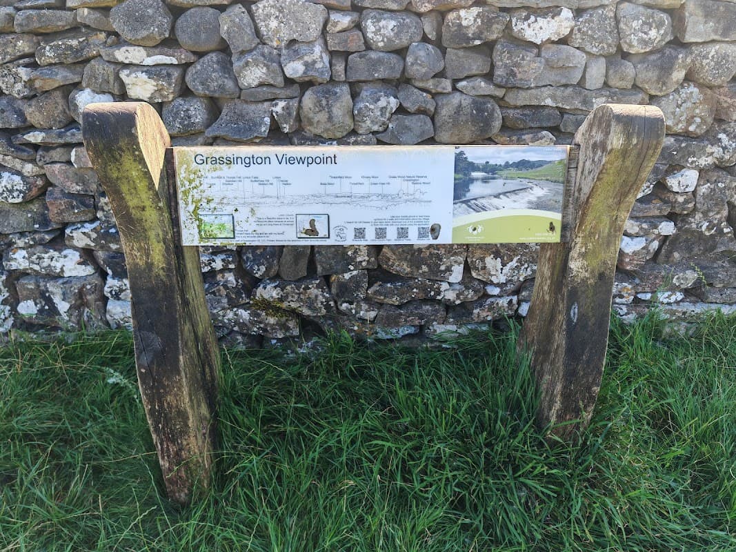 Signpost for Grassington Viewpoint, featuring a map and information, set against a stone wall and grassy area.