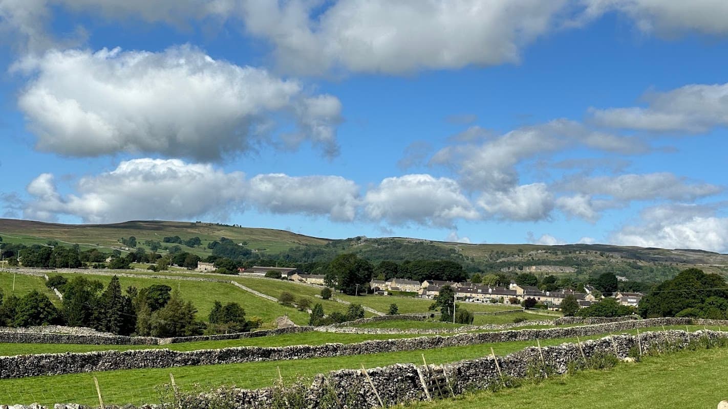 Scenic view of rolling hills and stone walls in Grassington, Yorkshire, with a backdrop of fluffy clouds and blue sky.