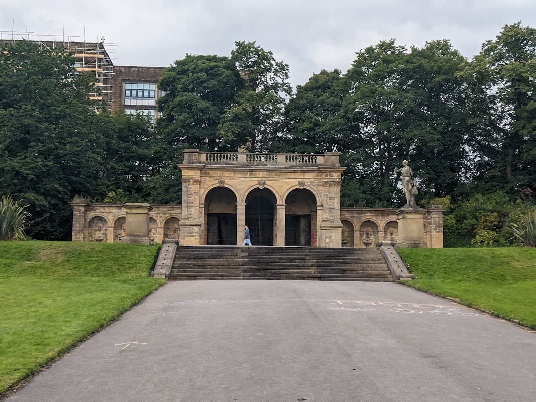 Historic stone structure with arches, steps, and a statue, surrounded by lush greenery in People's Park, Halifax.