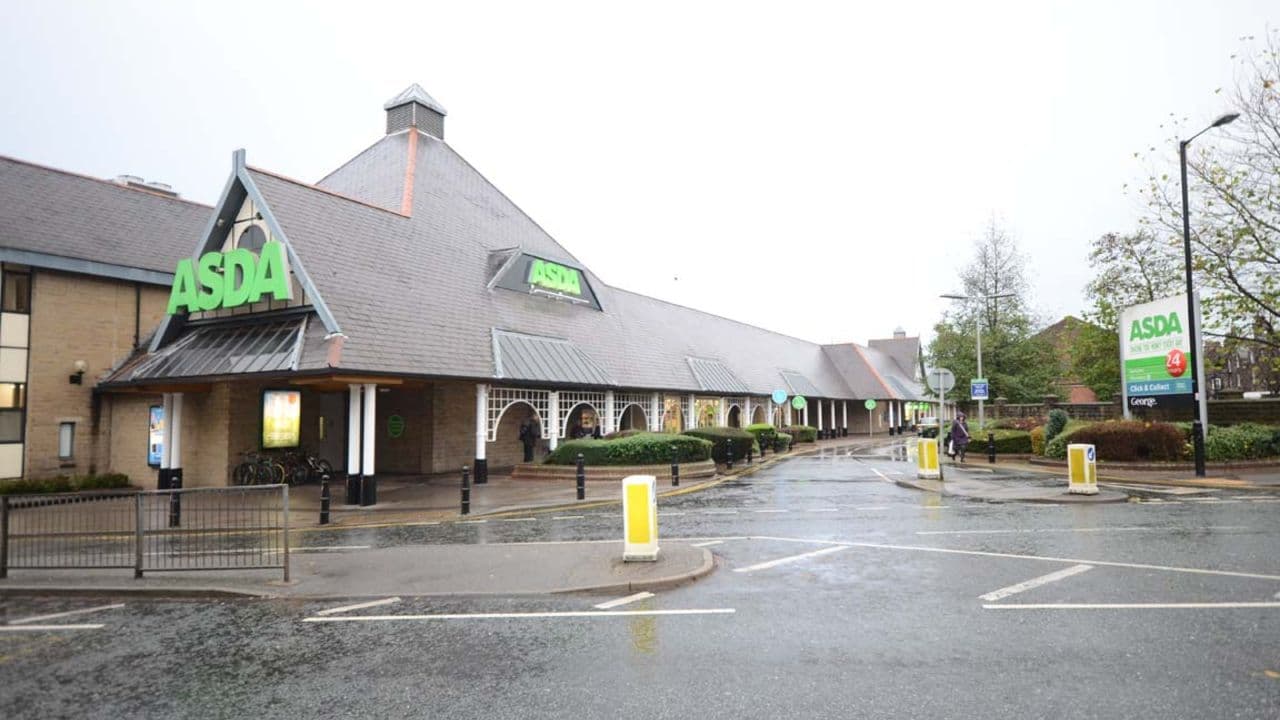 Asda Harrogate Superstore with a distinctive sloped roof, green signage, and a wet, reflective road in front.