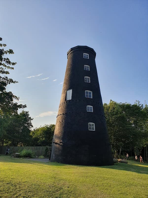 Black tower with windows, surrounded by green grass and trees under a clear blue sky.