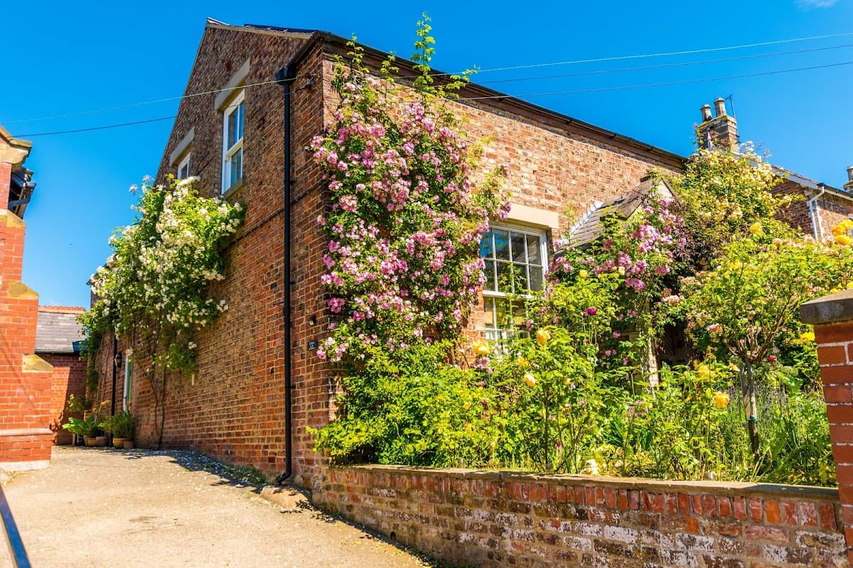 Charming brick building adorned with vibrant flowers and greenery under a clear blue sky in Husthwaite, Yorkshire.
