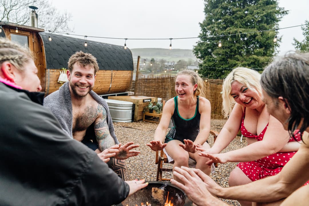 Group enjoying outdoor fire pit at iglu sauna with scenic countryside view
