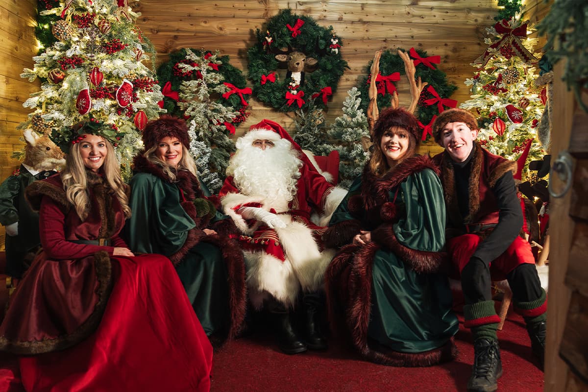 Festive grotto with Santa, surrounded by elves and decorated Christmas trees