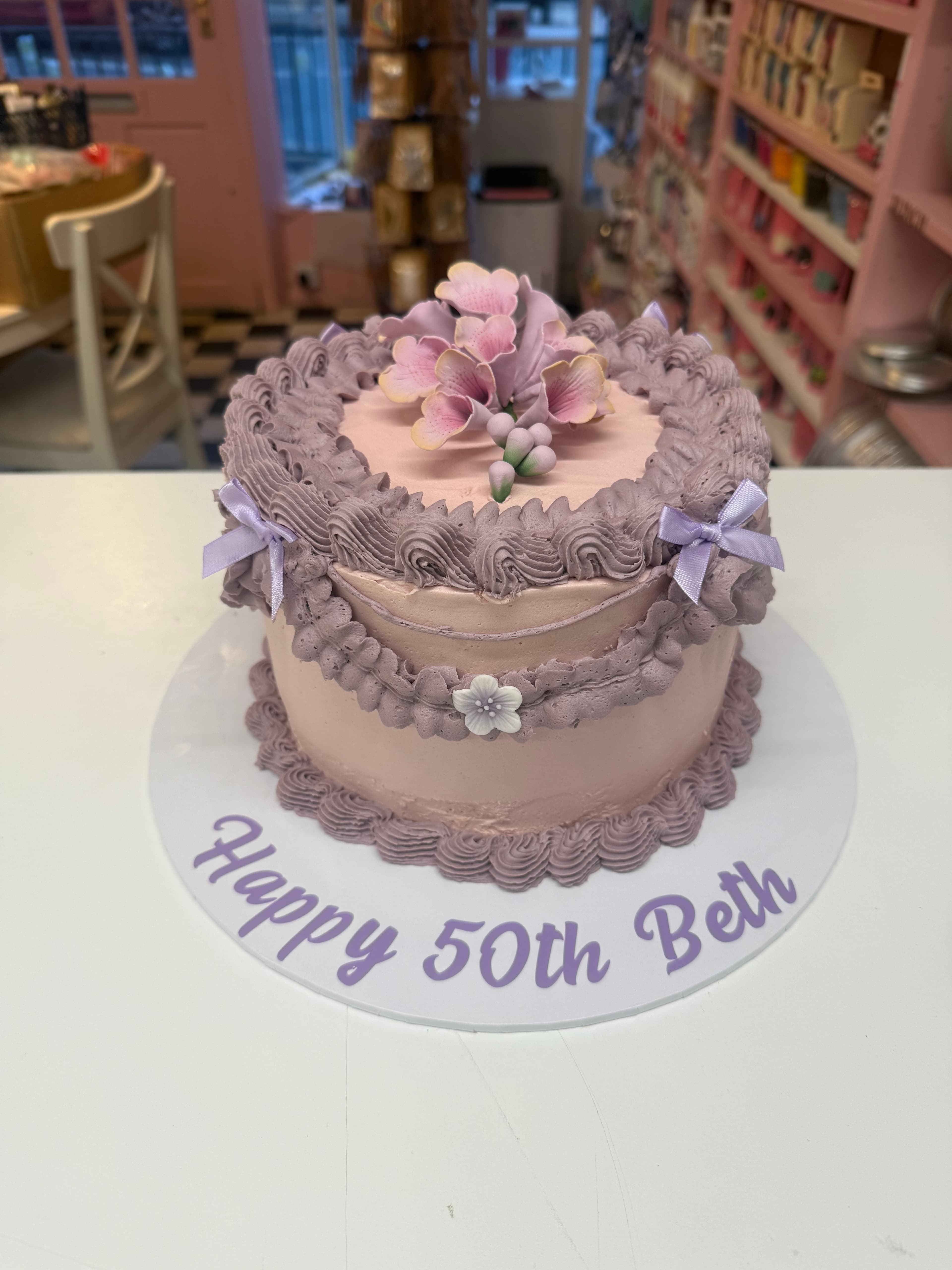Elegant pink and purple birthday cake with floral decorations on a display counter