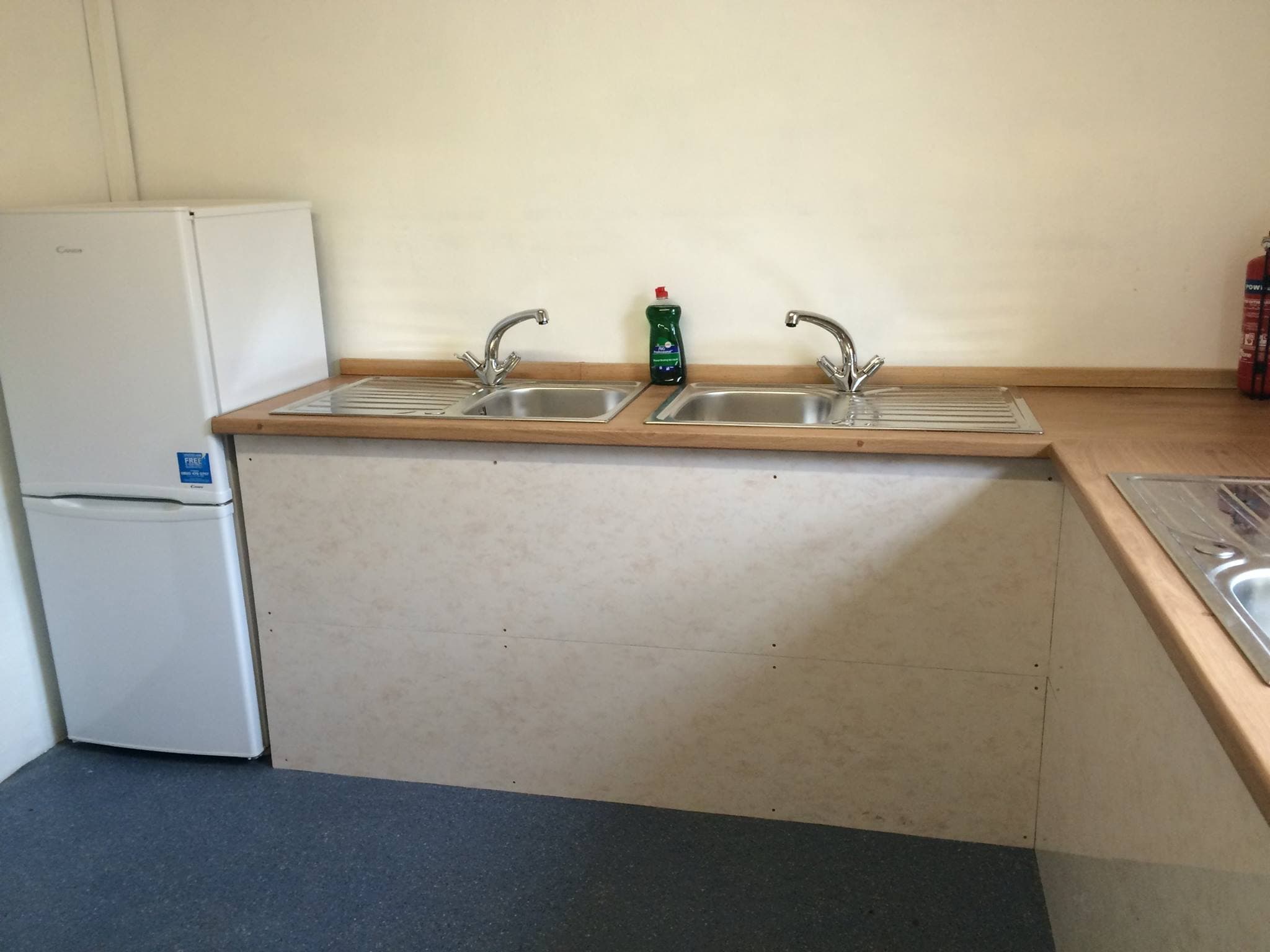 Campsite kitchen area with twin stainless steel sinks and a white refrigerator