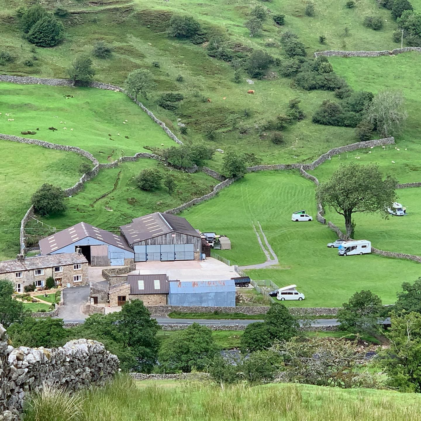 Scenic campsite with caravans, stone buildings, and lush green hills