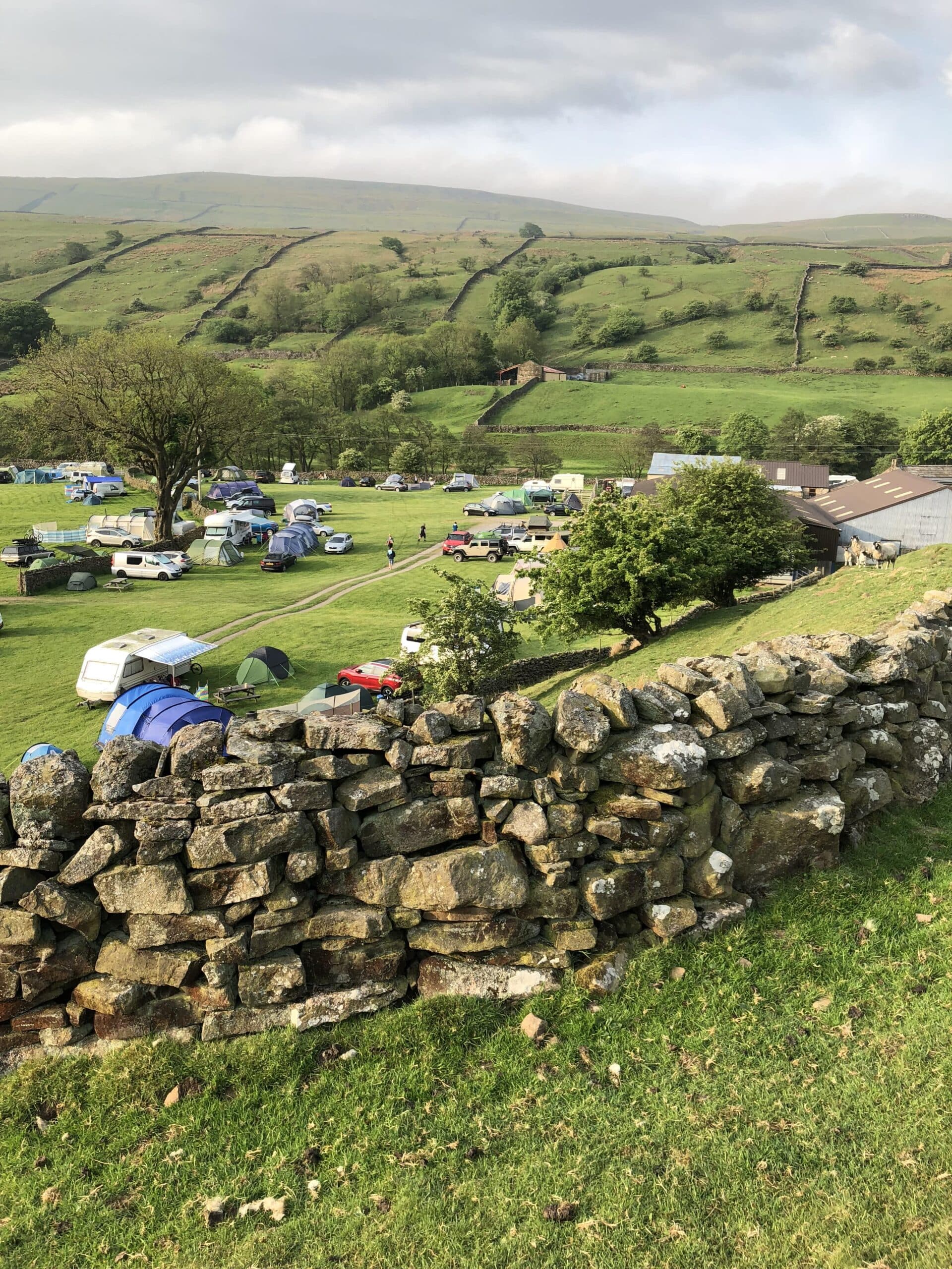 Scenic campsite with tents, caravans, and rolling hills in the background