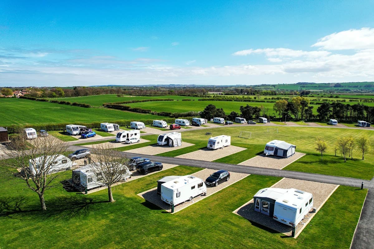 Caravan park with neatly arranged caravans on grassy plots, surrounded by green fields and blue sky in Lebberston, Yorkshire.