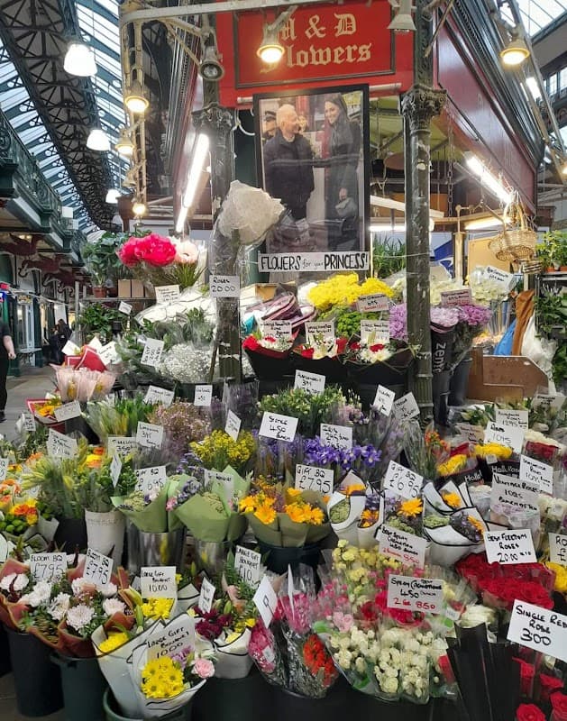 Colorful flower display with various bouquets, price tags, and a sign reading "M and D Flowers" in a market setting.