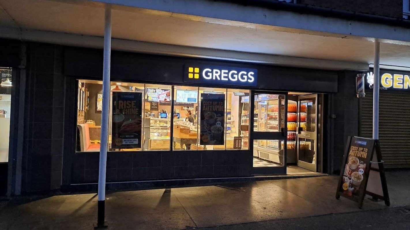 Greggs bakery storefront in Otley, Yorkshire, featuring illuminated signage and display of baked goods inside.