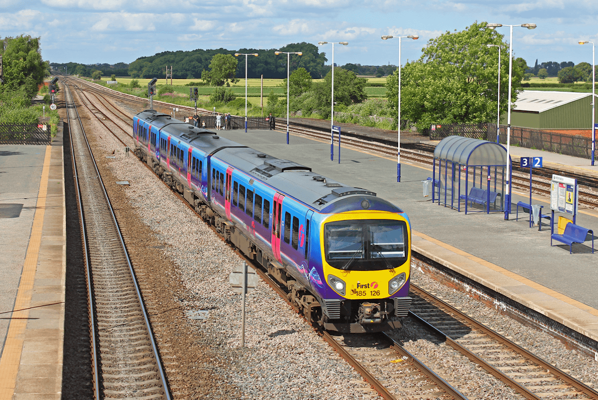 A train approaches Church Fenton station, with green fields and a clear blue sky in the background.