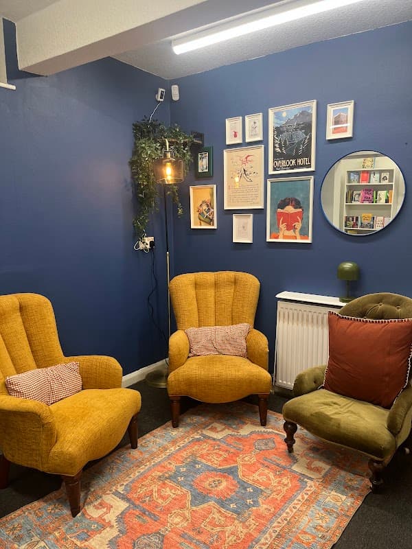 Cozy reading nook with yellow armchairs, green chair, colorful artwork, and a patterned rug against a blue wall.