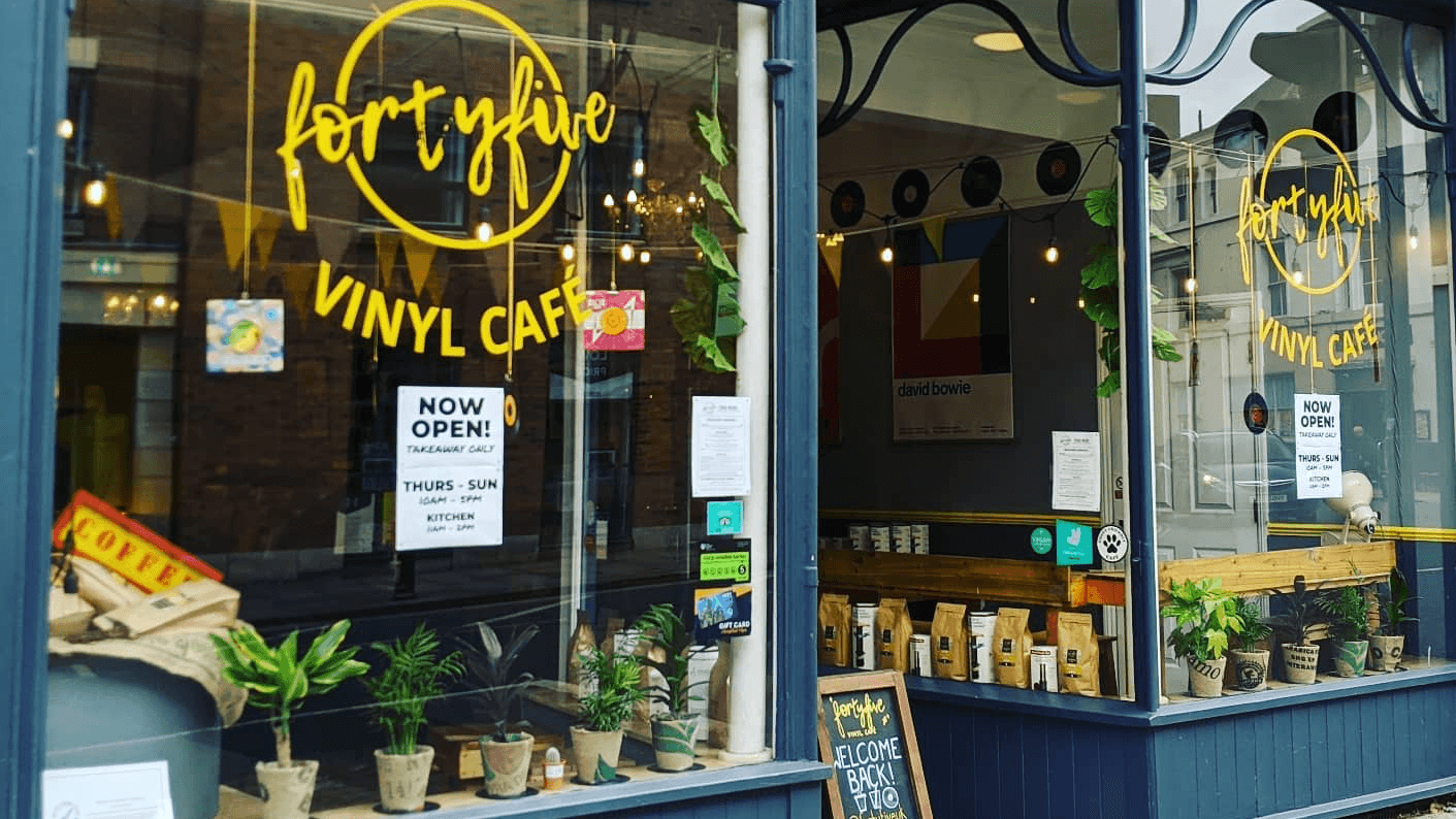 Vinyl cafรฉ storefront with large windows, plants, and a sign announcing "NOW OPEN" in York, Yorkshire.