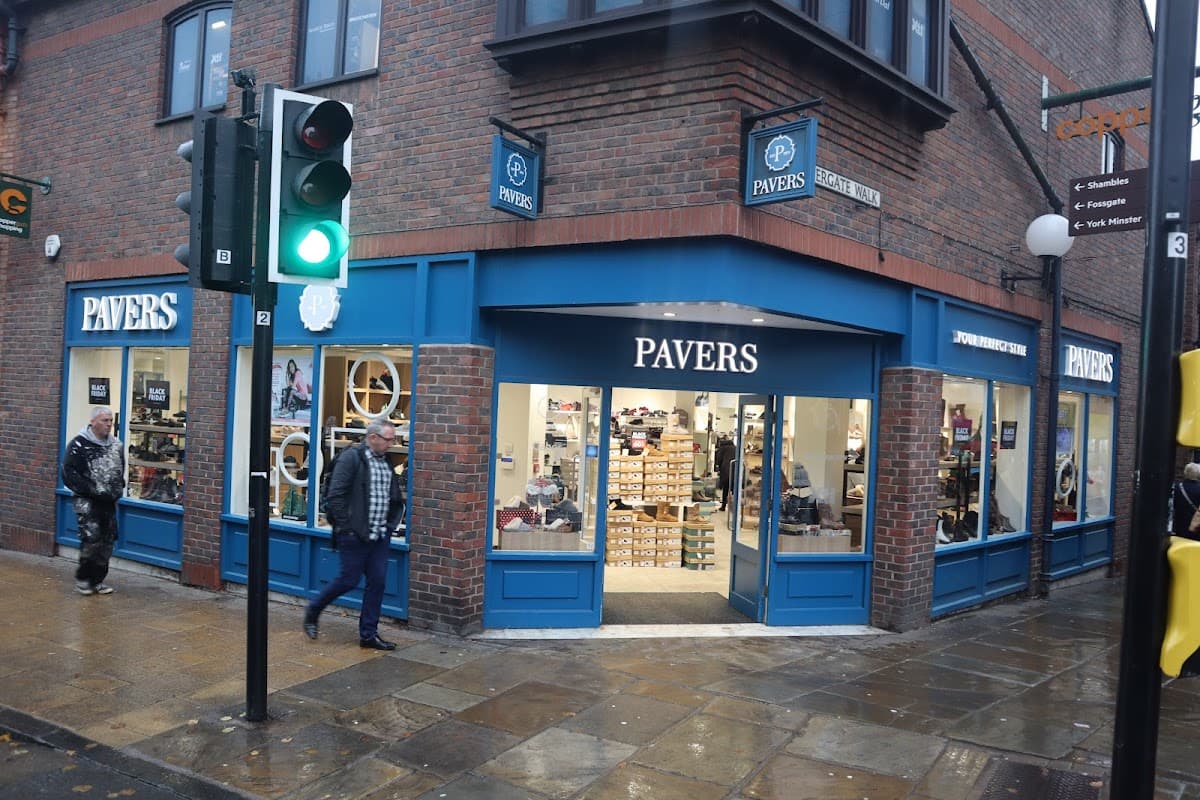 Pavers Shoes storefront with blue accents, large windows displaying shoes, and pedestrians outside in York, Yorkshire.