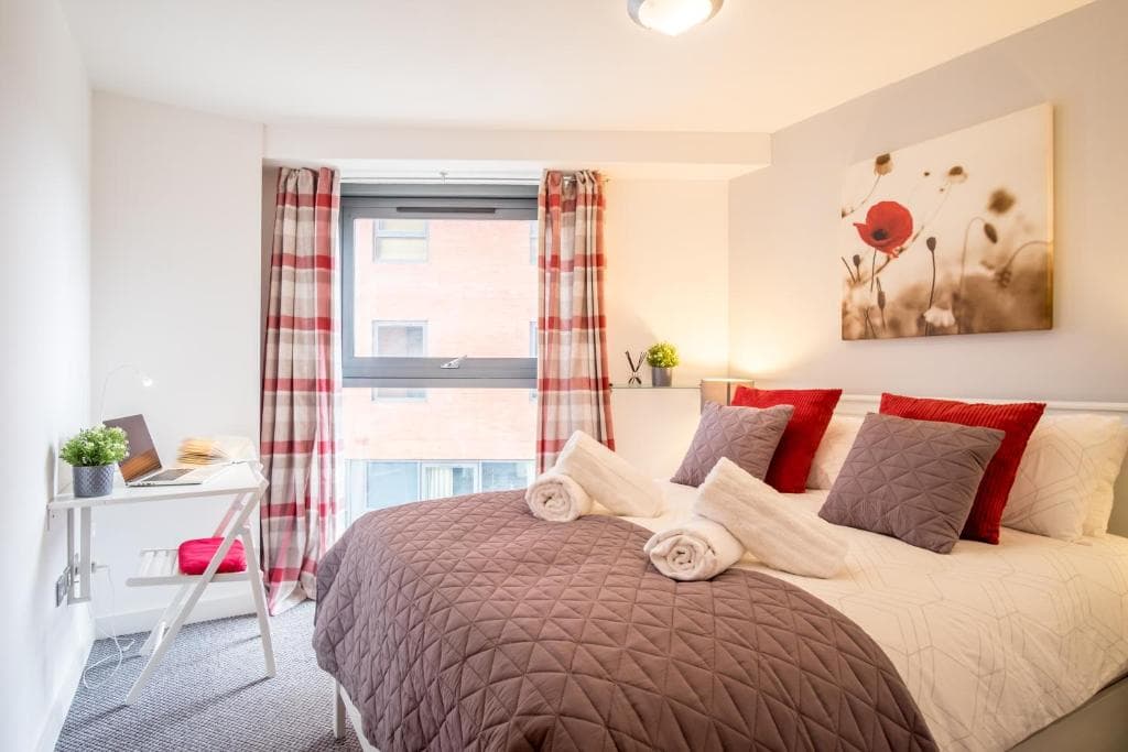 Stylish bedroom in Sheffield apartment, featuring a double bed, plaid curtains, wall art, and a desk with a laptop.