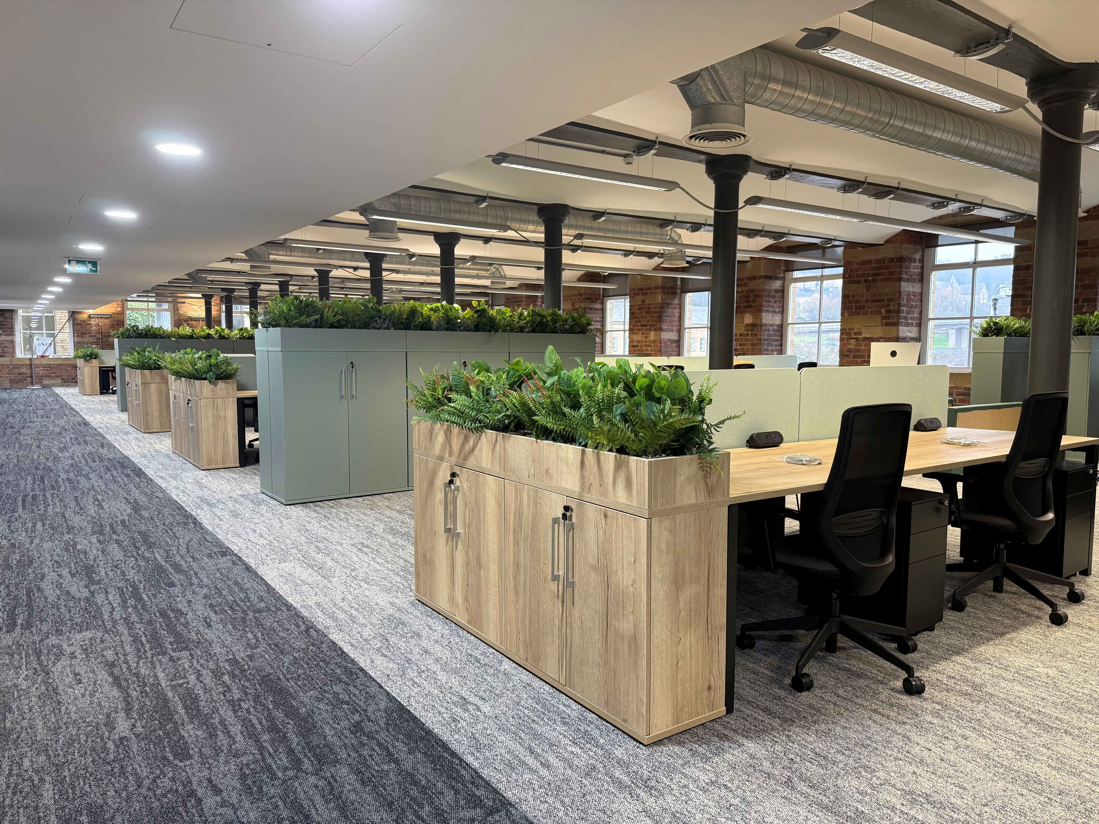 Modern office space in Dean Clough featuring greenery, open workstations, and exposed brick walls, creating an innovative atmosphere.