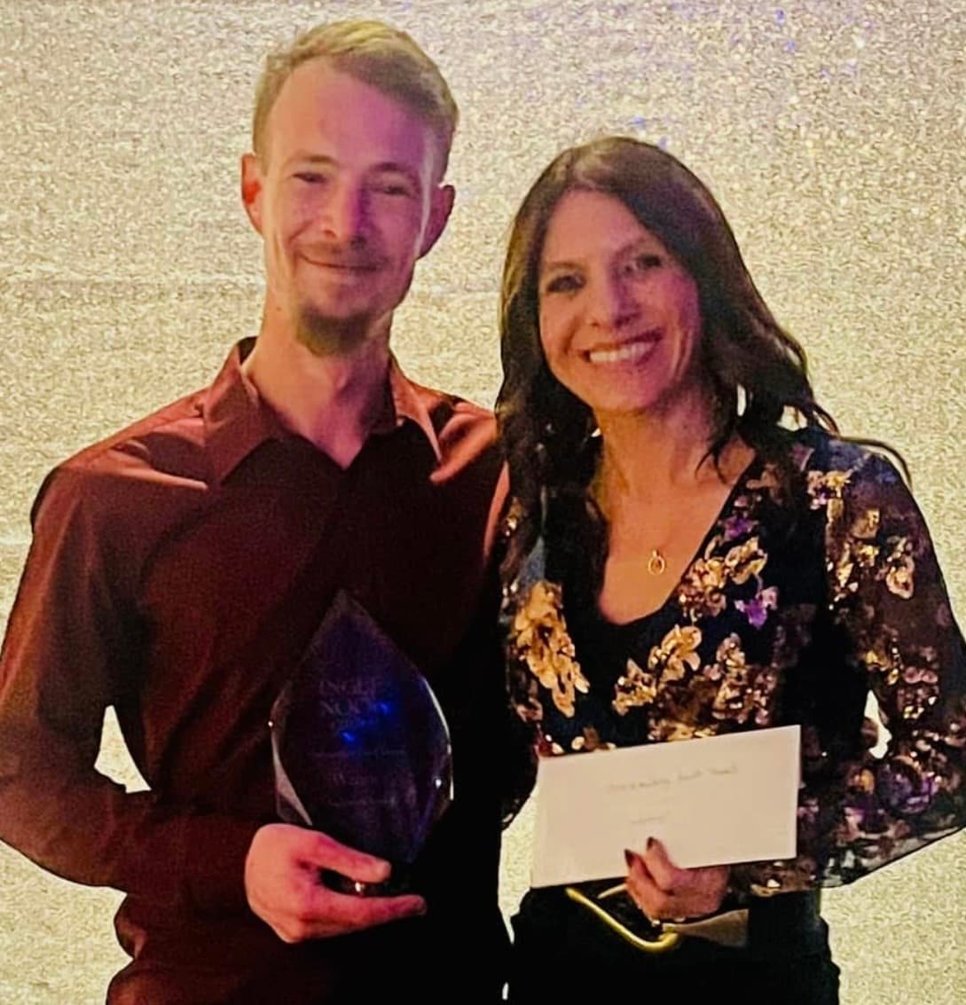 Two smiling individuals hold an award and an envelope, with a sparkling backdrop, celebrating a special occasion in Yorkshire.