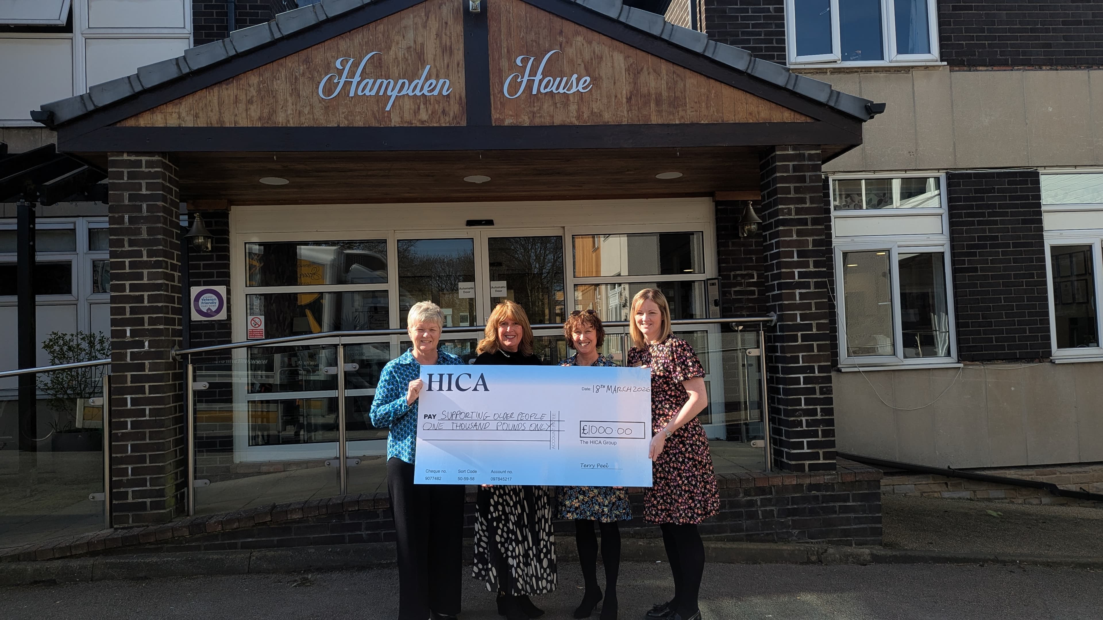 Four women stand outside Hampden House in Harrogate, holding a large cheque for £1,000 to support local befriending services.