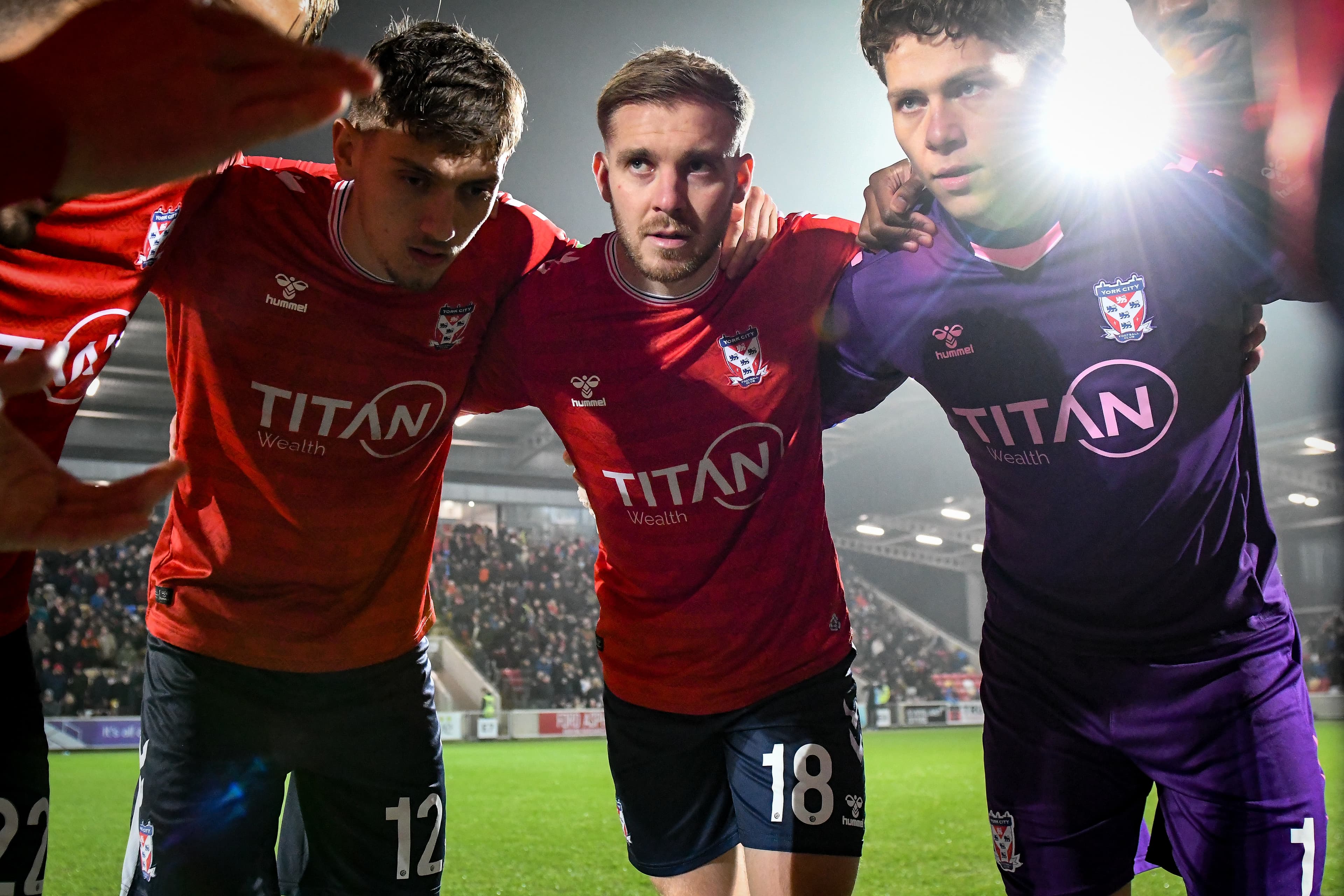 York City FC players in red jerseys huddle together on the pitch, illuminated by stadium lights, showcasing team spirit.
