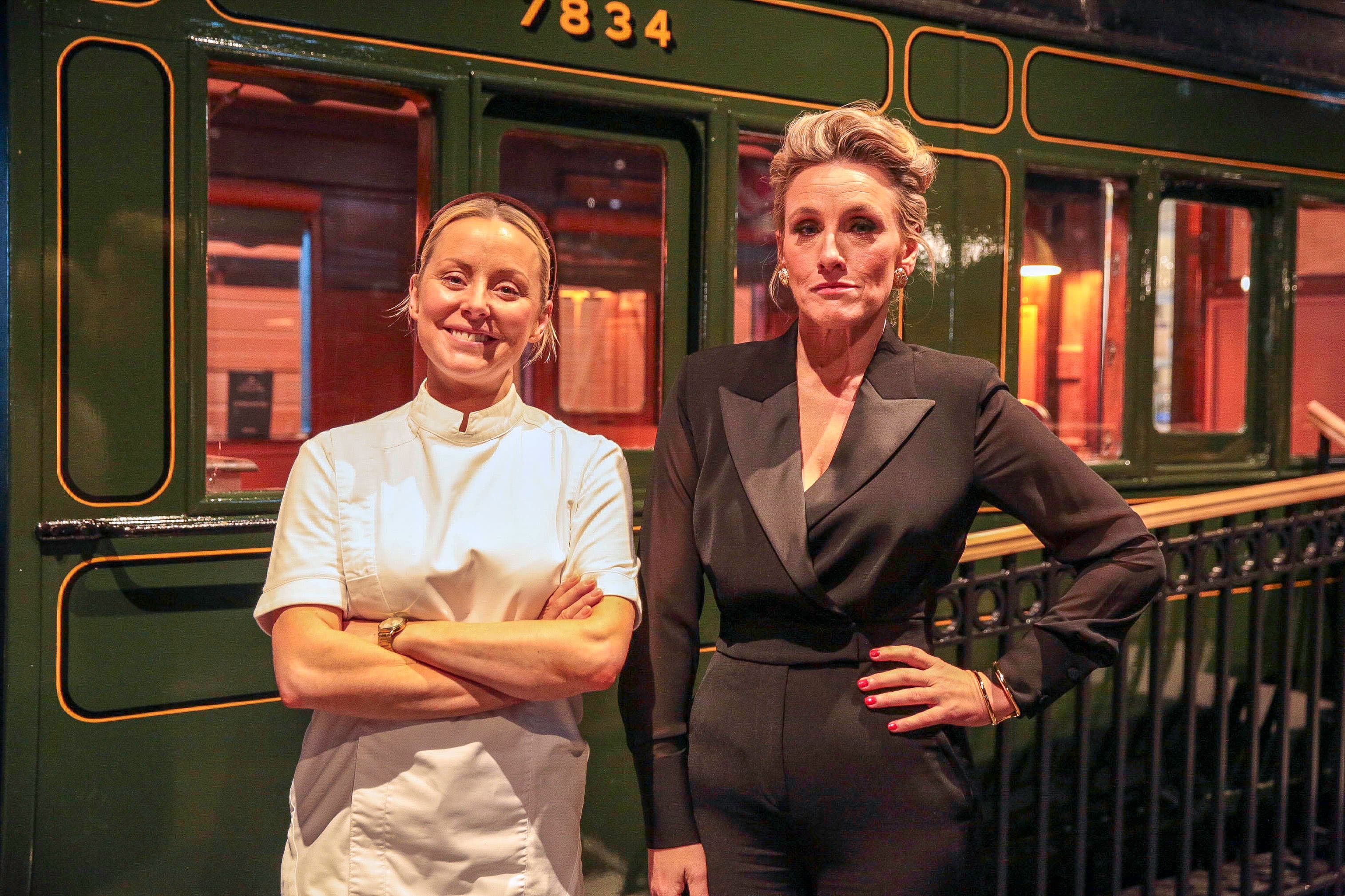 Two women standing in front of vintage green train carriage