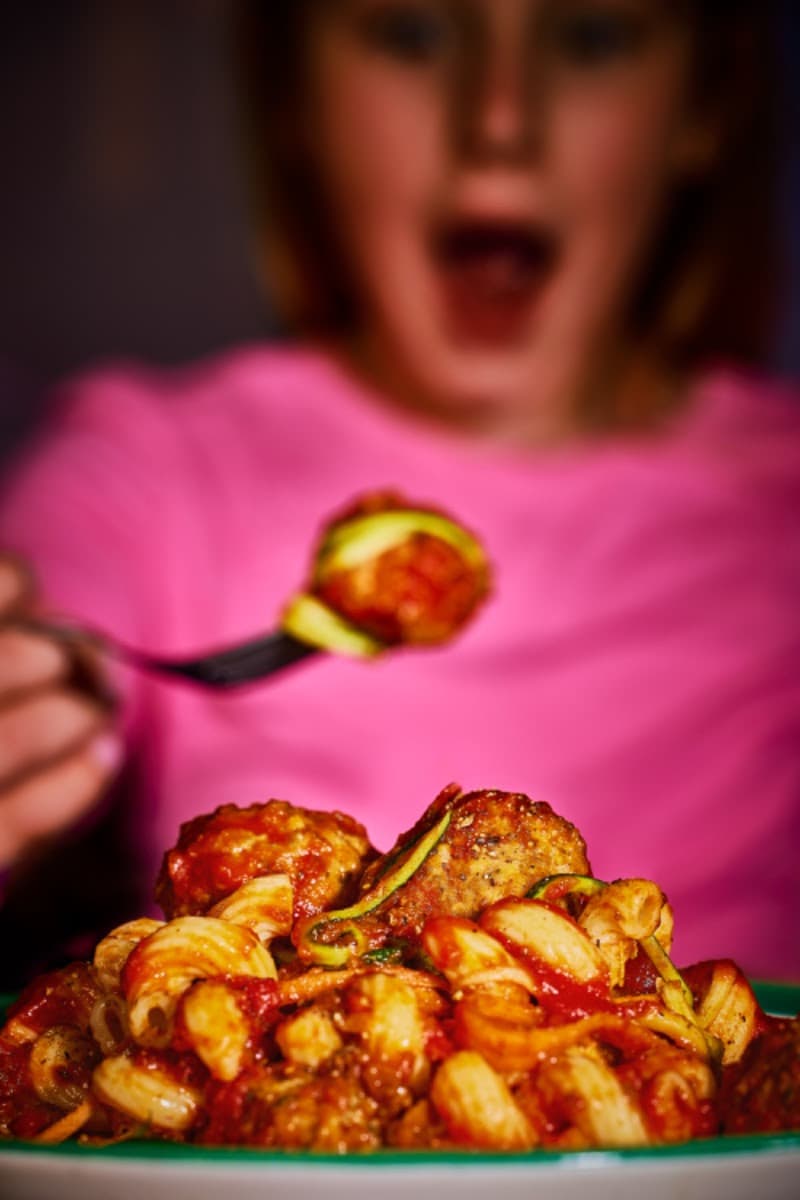 Child in pink shirt eating pasta with meatballs