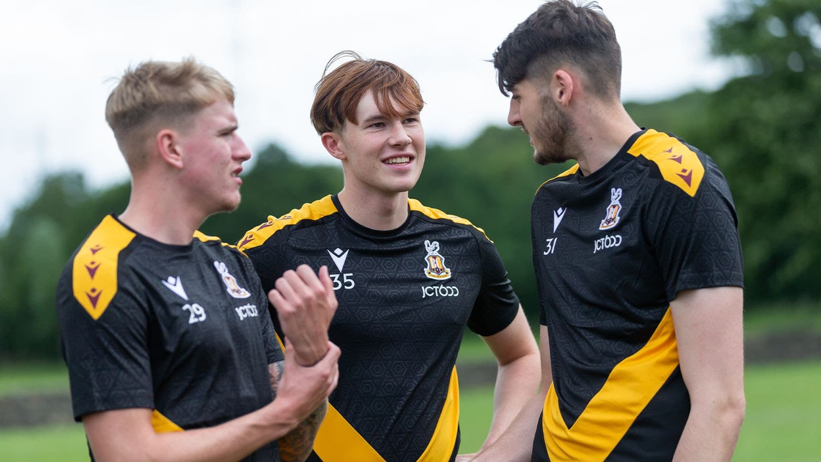 Three young men in black and yellow sports jerseys conversing outdoors