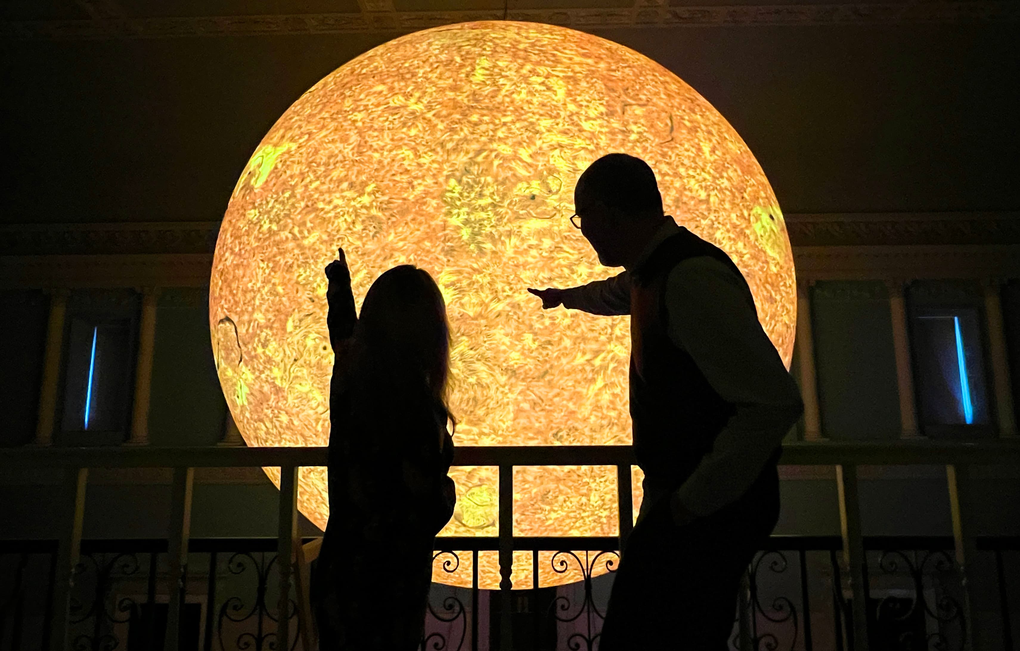 Two people silhouetted pointing at large illuminated sun model