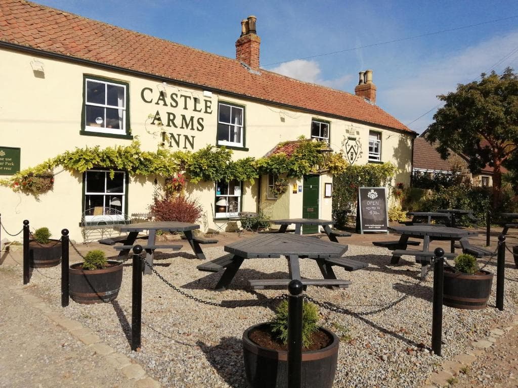 The Castle Arms Inn, a cozy bar with illuminated signage, outdoor seating, and lush greenery at night.