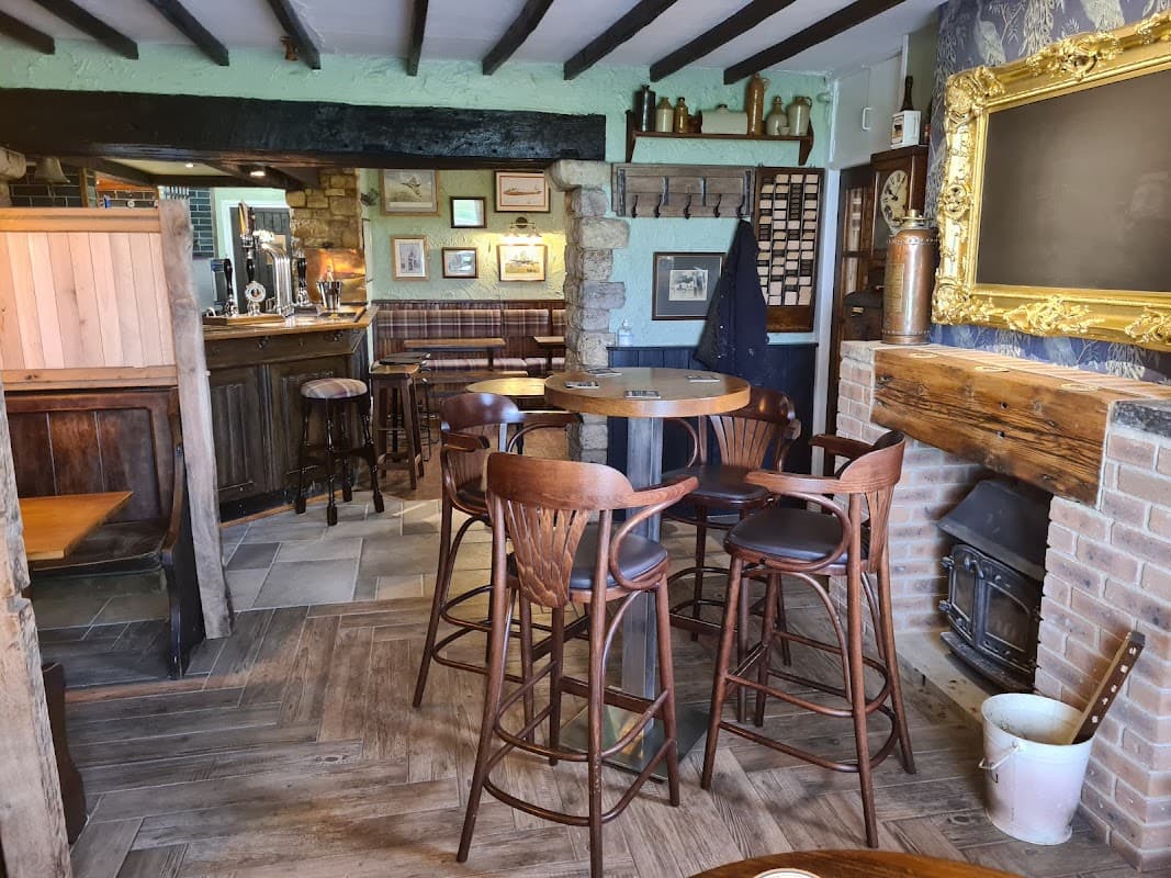Cozy pub interior with wooden bar stools, a rustic bar, stone walls, and a fireplace, creating a warm atmosphere.
