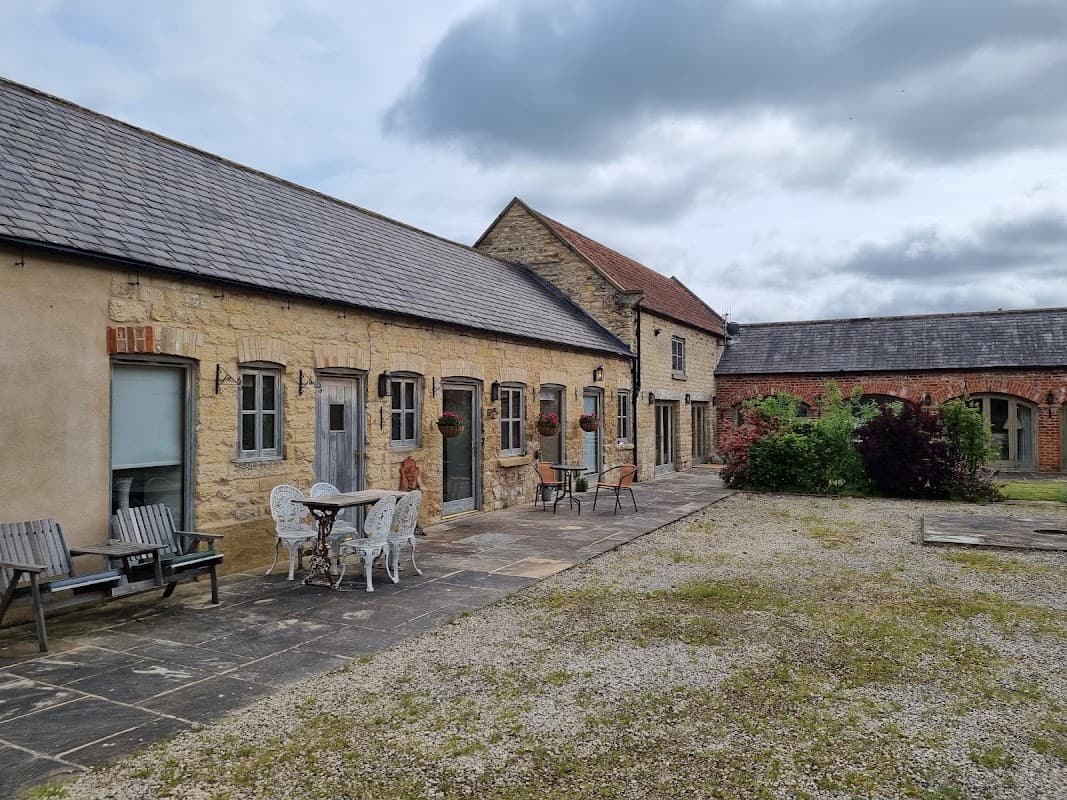 Stone cottage with outdoor seating, planters, and a gravel courtyard under a cloudy sky in Barton-le-Street, Yorkshire.