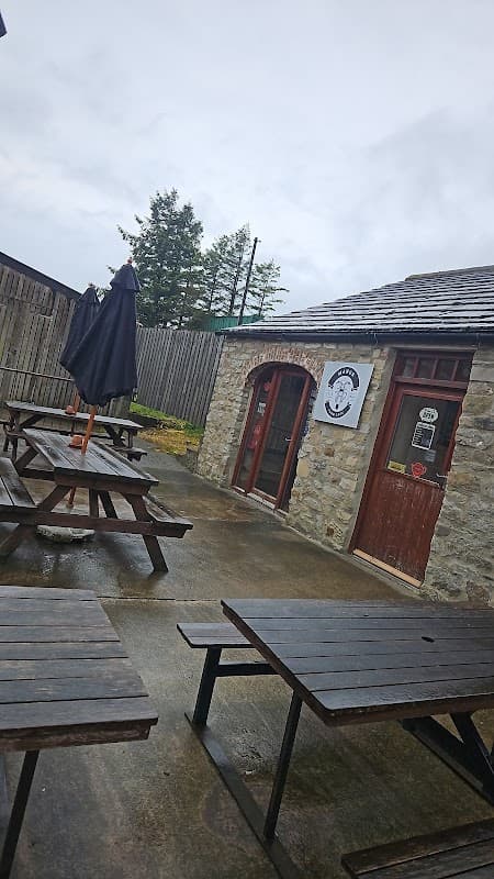 Stone building with wooden picnic tables outside, an umbrella, and a sign for "The Manor Farm Cafe" in Bellerby.
